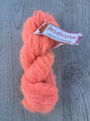 Ein fluffiger, handgefärbter Strang Wolle in leuchtendem Korallorange mit feinen rosa und apricotfarbenen Nuancen. Der Strang liegt auf hellem Holz. Das Garn wirkt weich, flauschig und leicht glänzend.
